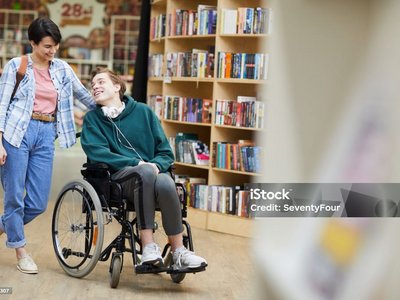 Rollstuhlfahrer und eine junge Dame lachend in der Bibliothek.