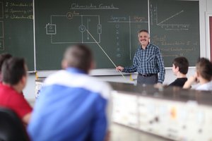 Ausbilder erklärt etwas an der Tafel und erklärt lächelt Schüler an.