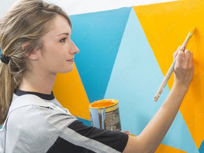 Mädchen bemalt eine Wand in bunten Farben.